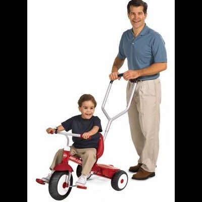 Triciclo infantil vermelho com barra de empurrar e criança sentado, adulto ao lado