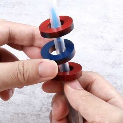 Caneta transparente com tinta azul e três anéis coloridos nas mãos sobre fundo cinzento claro.