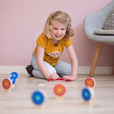 Menina brincando com brinquedos de madeira no chão junto a uma cadeira cinza