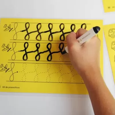 Folha amarela com exercícios de caligrafia com padrão de laços desenhados e mão de criança a usar marcador preto