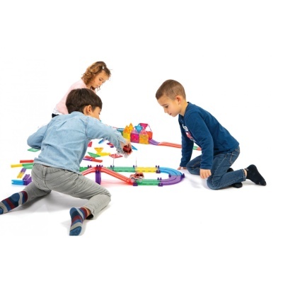 Crianças a brincar com pistas modulares de brinquedo coloridas no chão branco.