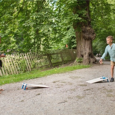 Crianças a jogar cornhole ao ar livre com tábuas brancas e sacos coloridos