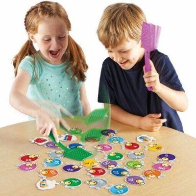 Duas crianças a jogar com peças redondas coloridas numeradas numa mesa de madeira clara