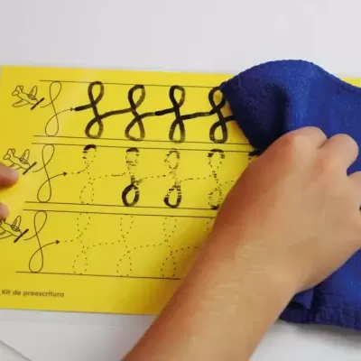 Folha amarela de treino de escrita cursiva com mãos e pano azul