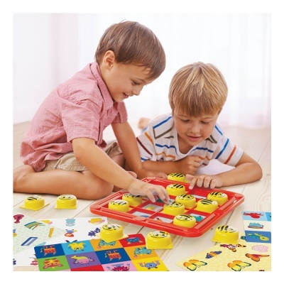 Crianças a jogar jogo de tabuleiro com fichas amarelas sorridentes e cartas coloridas num chão de madeira