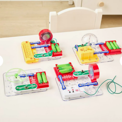 Quatro kits de circuitos eletrónicos educativos com vários componentes coloridos sobre mesa branca