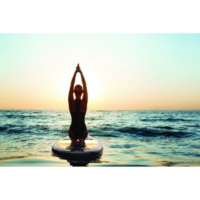 Mulher de costas em fato de banho preto sentada em prancha de stand up paddle ao pôr do sol