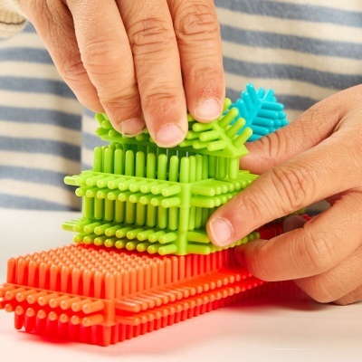 Peças de plástico coloridas com pinos manuseadas por mãos sobre mesa branca.