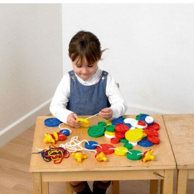 Menina a brincar com brinquedo colorido de enfiar em mesa de madeira