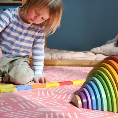 Criança a brincar com blocos de construção e arco-íris de madeira coloridos sobre tapete