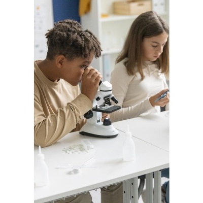 Duas crianças usando equipamento de ciência numa mesa branca.
