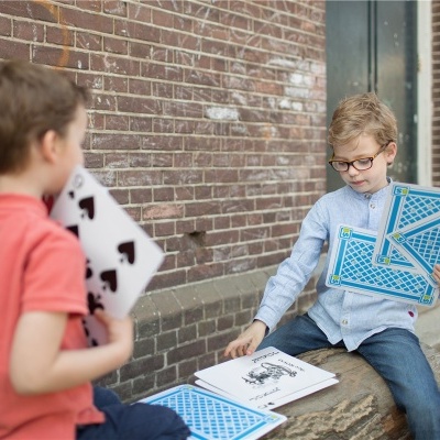 Duas crianças com cartas gigantes junto a uma parede de tijolos e livro aberto