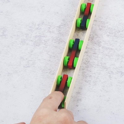 Carris de brinquedo de madeira com rodas verdes numa estrutura longa de madeira clara, mão a tocar numa carruagem.