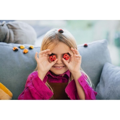 Menina loira com brinquedos de joaninhas vermelhas e pretas no rosto e no sofá cinzento