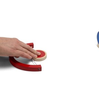 Mesa de jogo com discos de madeira vermelhos e azuis, mão a lançar disco vermelho.