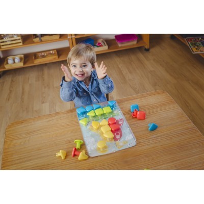 Criança brincando com peças de plástico coloridas sobre mesa de madeira, em sala de aula