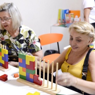 Tabuleiros de madeira com blocos coloridos em mesa branca com duas mulheres sentadas