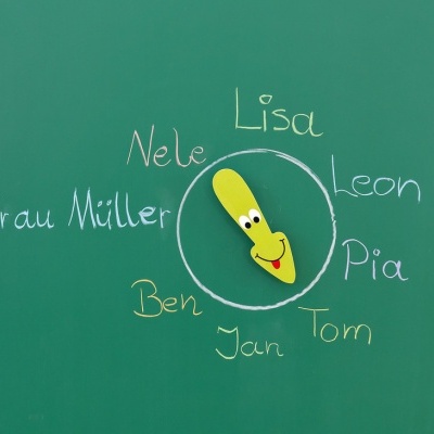 Quadro verde com nomes escritos a giz colorido e marcador amarelo sorridente