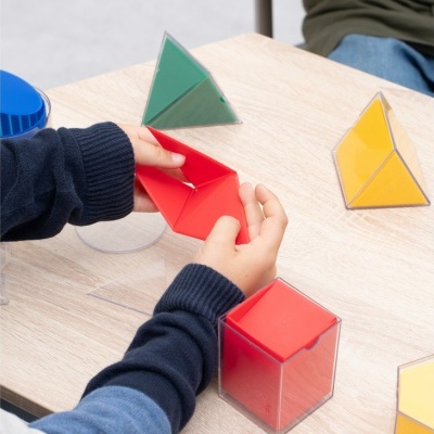 Formas geométricas coloridas em cima de uma mesa de madeira clara, incluindo pirâmides e cubo.