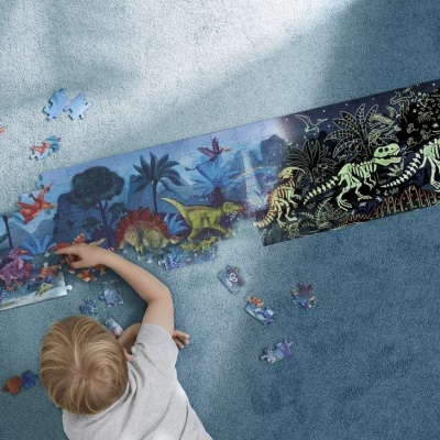 Criança a montar puzzle educativo de dinossauros colorido e com esqueletos sobre tapete azul.