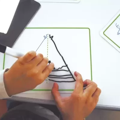 Mãos infantis a desenhar numa placa branca magnética com marcador preto