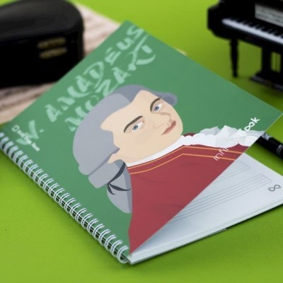 Caderno espiral verde com desenho de Mozart e texto sobre superfície verde
