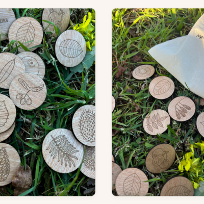 Peças de madeira redondas com desenhos de folhas, plantas e texto, em relva junto a um saco de pano