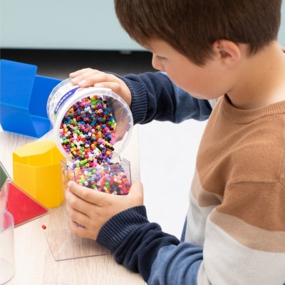 Menino a verter contas de plástico coloridas entre recipientes sobre uma mesa com organizadores coloridos