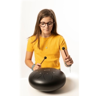 Tambor de aço negro com seis lengalengas e baquetas, usado por rapariga com camisola castanha amarela.