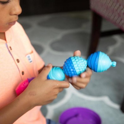 Criança a segurar brinquedos de plástico azul com texturas sentado em tapete cinzento
