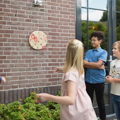 Crianças brincando de arremessar dardos num alvo de madeira numa parede de tijolos