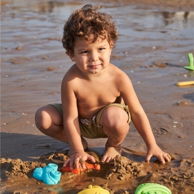 Criança de calções verdes a brincar com brinquedos de praia coloridos na areia