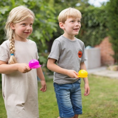Duas crianças seguram colheres coloridas num jardim verde