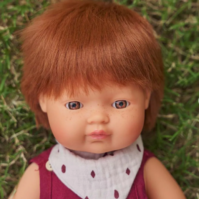 Boneca com cabelo castanho-avermelhado e vestido roxo deitada na relva