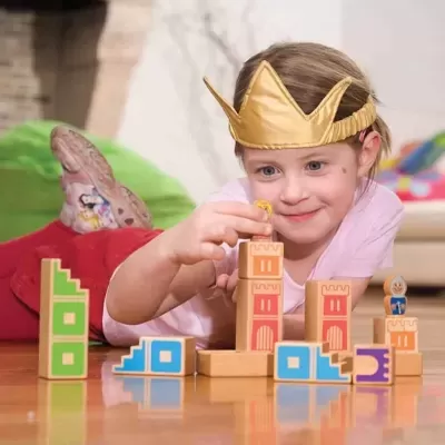 Criança a jogar com blocos de madeira coloridos usando uma coroa dourada.