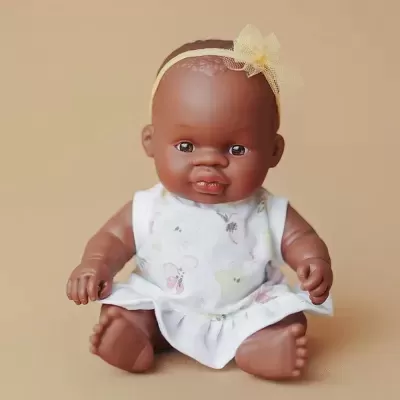 Boneca bebé com roupa branca estampada e fita amarela na cabeça
