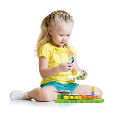 Menina loira brincando com brinquedo de construção colorido sentada no chão branco