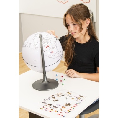 Globo terrestre branco em suporte cinza com marcadores e folha com bandeiras e animais na mesa