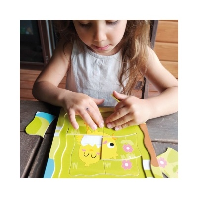 Criança a montar um quebra-cabeças de madeira com imagens coloridas de animais numa mesa de madeira