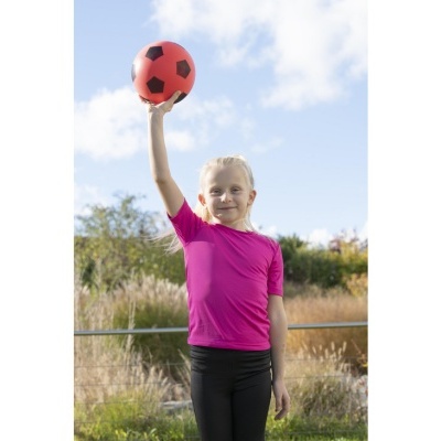 Criança loira segurando bola vermelha com hexágonos pretos no ar ao ar livre