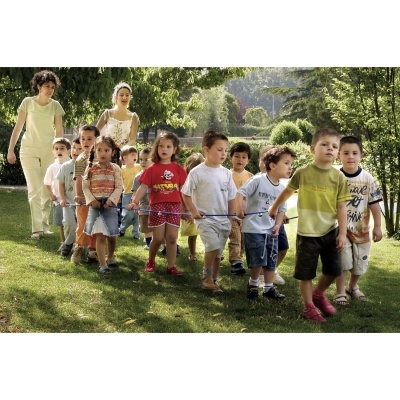 Crianças pequenas e educadoras a caminhar ao ar livre ligadas por uma corda num parque verde