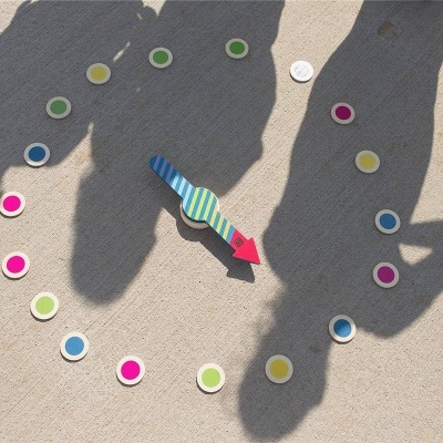 Relógio de madeira colorido com ponteiro azul e vermelho sobre areia clara com sombras