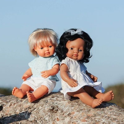 Duas bonecas de vinil sentadas num tronco de árvore ao ar livre