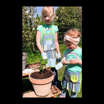 Crianças a fazer jardinagem com aventais e luvas junto de vaso com planta