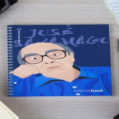 Caderno com capa ilustrada de José Saramago em azul, branco e bege, em secretária clara com máquina de escrever e chávena de café