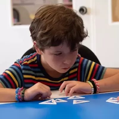 Criança com camisola colorida e pulseiras a mexer em cartas triangulares numa mesa azul