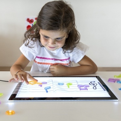 Criança usando tablet iluminado com peças de plástico coloridas em forma de letras e números