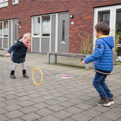 Crianças a brincar ao ar livre numa rua com prédios e chão de pedras.