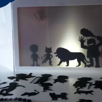Caixa luminosa branca com figuras recortadas de sombras de personagens e animais.