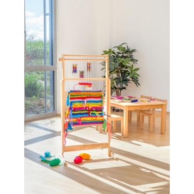 Cadeira infantil de madeira com assento multicolorido num ambiente luminoso com mesa e planta